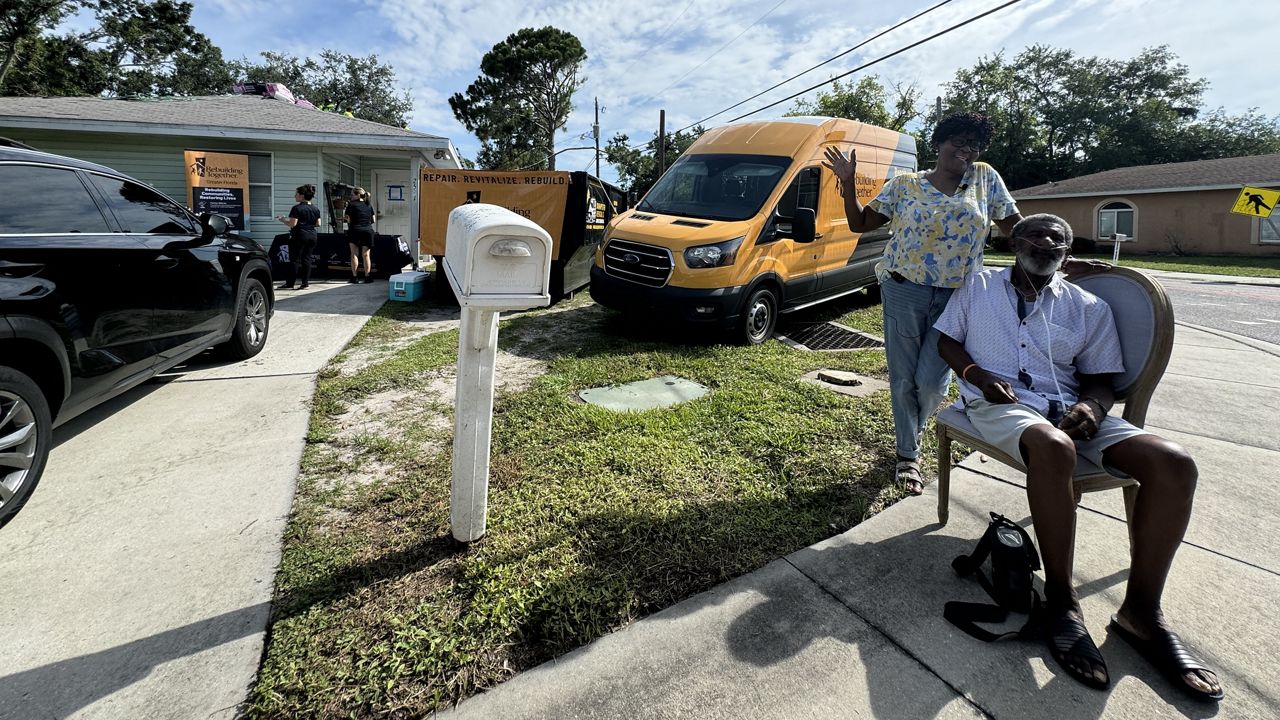 Husband and wife Shelia Cantrell (left) and Johnnie Cantrell sit in front of their home while they watch workers build them a new roof. (Spectrum News)