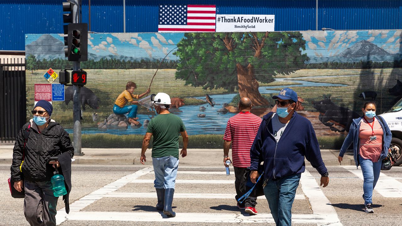 FILE - In this Thursday, May 21, 2020, photo, Farmer John workers wear face mask as they walk to the plant in Vernon, Calif. The state is still seeing troubling COVID-19 flare-ups, however. More than 150 employees at a Farmer John meatpacking plant in Vernon, an industrial city five miles south of downtown Los Angeles, contracted the coronavirus. (AP Photo/Damian Dovarganes, File)