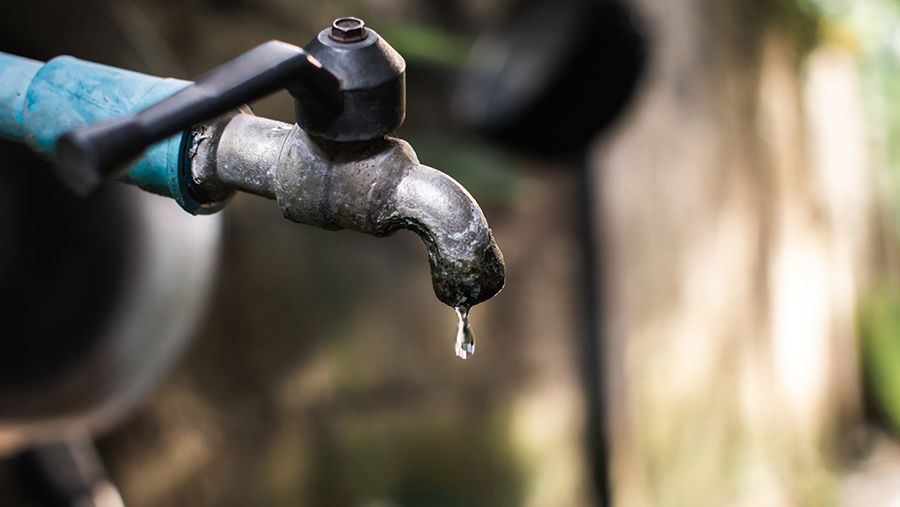 Old faucet with water leaking drop to the ground.