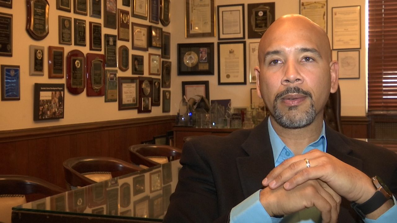 Bronx Borough President Ruben Diaz Jr., wearing a black blazer and a teal dress shirt, sits in an office.