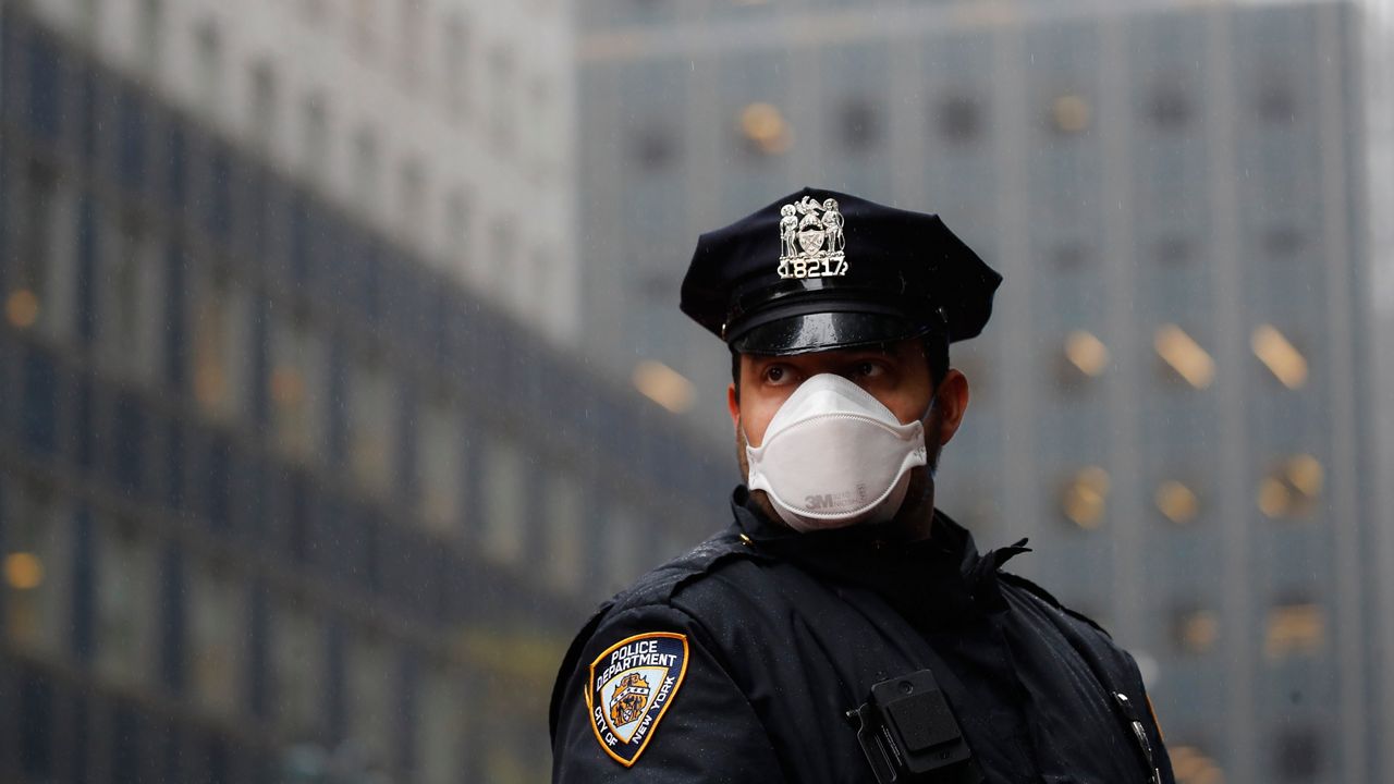 NYPD officer wearing a black uniform, hat, and a white mask