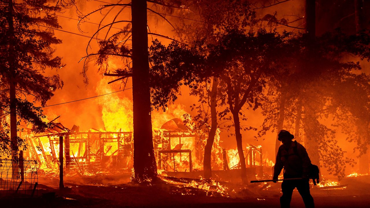 A firefighter passes a burning home as the Dixie Fire flares in Plumas County, Calif. (AP/Noah Berger)