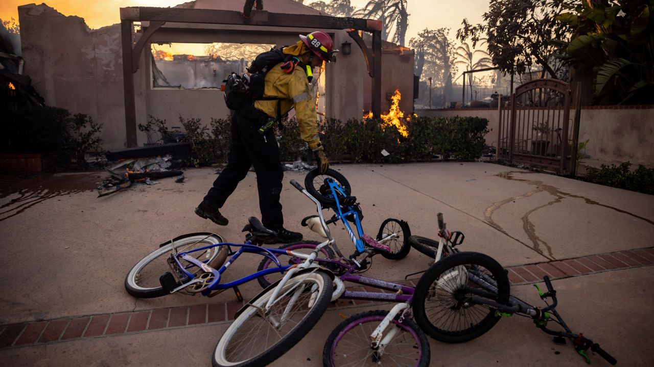 A firefighter, moves bicycles as he works against the Mountain fire on Wednesday near Camarillo, Calif. (AP Photo/Ethan Swope)