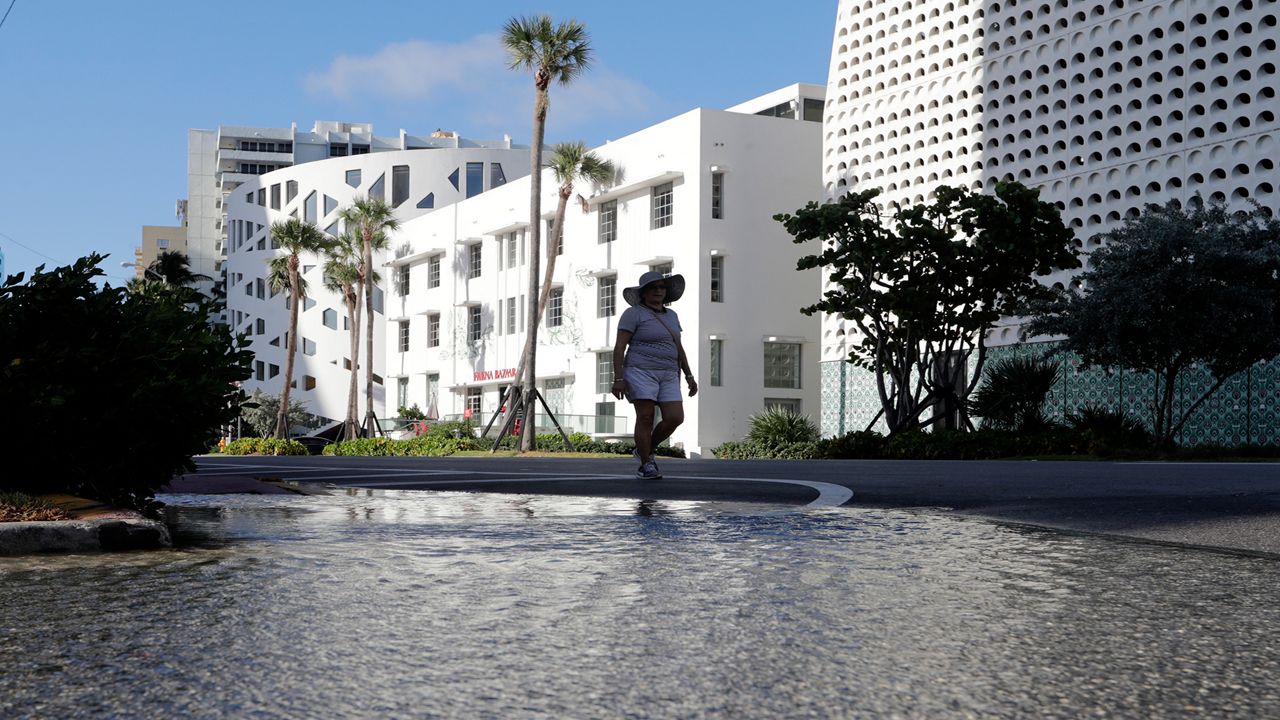 A woman walks along a flooded street caused by a king tide, Saturday, Sept. 28, 2019, in Miami Beach, Fla. Low-lying neighborhoods in South Florida are vulnerable to the seasonal flooding caused by king tides. (AP Photo/Lynne Sladky)
