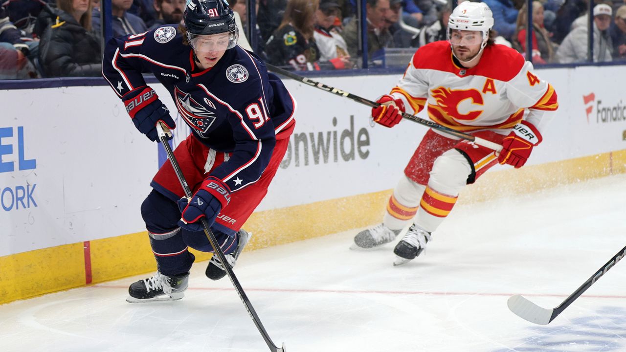 Columbus Blue Jackets forward Kent Johnson, left, controls the puck in front of Calgary Flames defenseman Rasmus Andersson during an NHL hockey game in Columbus, Ohio, Friday, Nov. 29, 2024. The Blue Jackets won 5-2. (AP Photo/Paul Vernon)