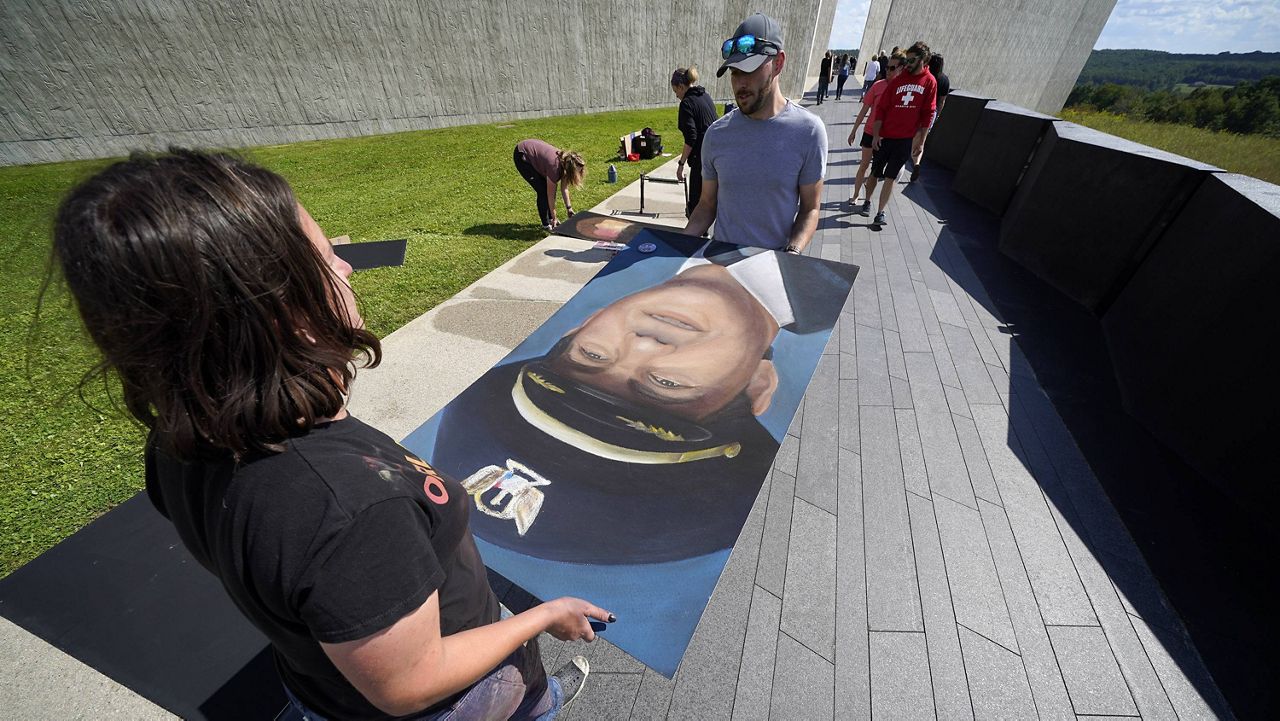 Chalk artist Naomi Haverland helps move a portrait Thursday of Flight 93 Capt. Jason M. Dahl along the flight path that leads to the Flight 93 National Memorial in Shanksville, Pa. (AP Photo/Gene J. Puskar)