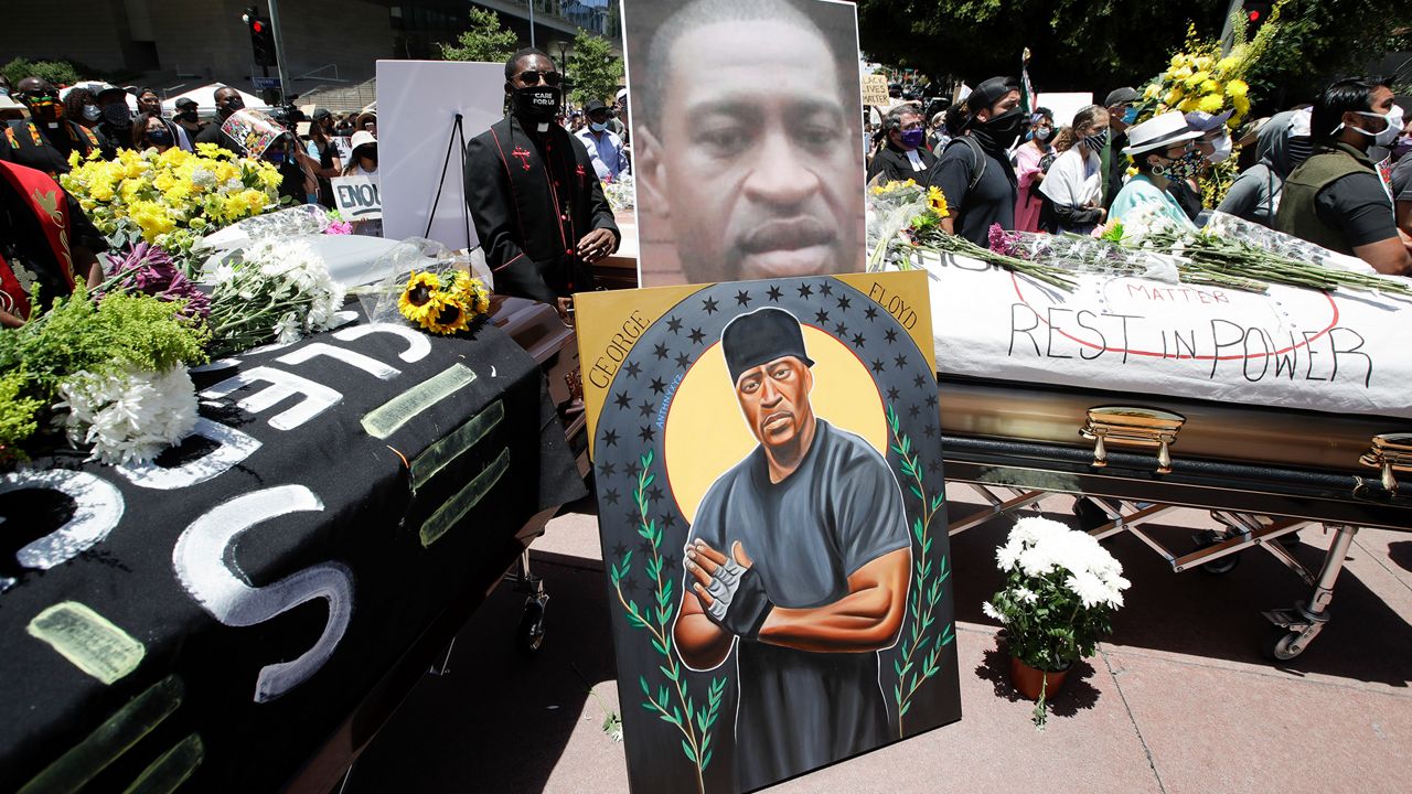 Pastor Eddie Anderson, center, of McCarty Memorial Church, stands behind caskets and and image of George Floyd, Monday, June 8, 2020, in Los Angeles during a protest over the death of Floyd on May 25 after he was restrained by Minneapolis police.. (AP Photo/Marcio Jose Sanchez)