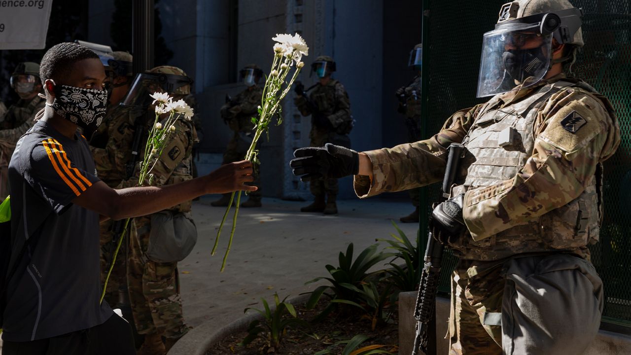 A demonstrator offers flowers to a National Guardsman stationed outside the office of Los Angeles County District Attorney Jackie Lacey, Wednesday, June 3, 2020, in Los Angeles, during a protest over the death of George Floyd, who died May 25 after being restrained by police in Minneapolis. (AP Photo/Damian Dovarganes)