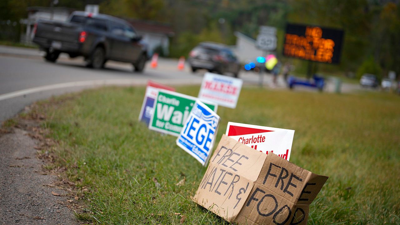 FILE - A makeshift cardboard sign leans up against campaign posters near a relief center on Oct. 3, 2024, in Vilas, N.C. in the aftermath of hurricane Helene. (AP Photo/Chris Carlson, file)