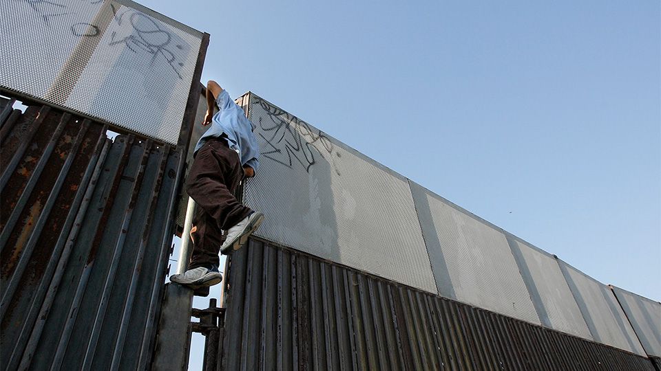 A person climbs a border fence in this undated AP Image (Photo Credit: Associated Press)