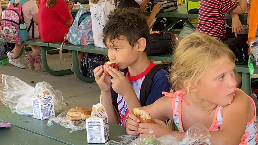 a boy and girl eating lunch on a bench