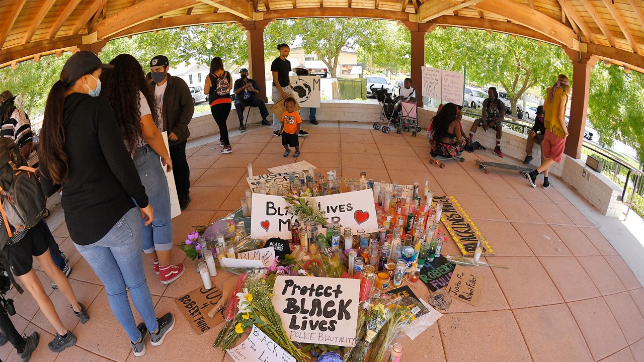 People look at a memorial as they gather at the site where Robert Fuller was found hanged, Monday, June 15, 2020, in Palmdale, Calif. State and federal authorities will monitor the investigation into the death of Fuller, a black man found hanging from a tree in the Southern California city of Palmdale, officials said Monday following large weekend protests. (AP Photo/Mark J. Terrill)