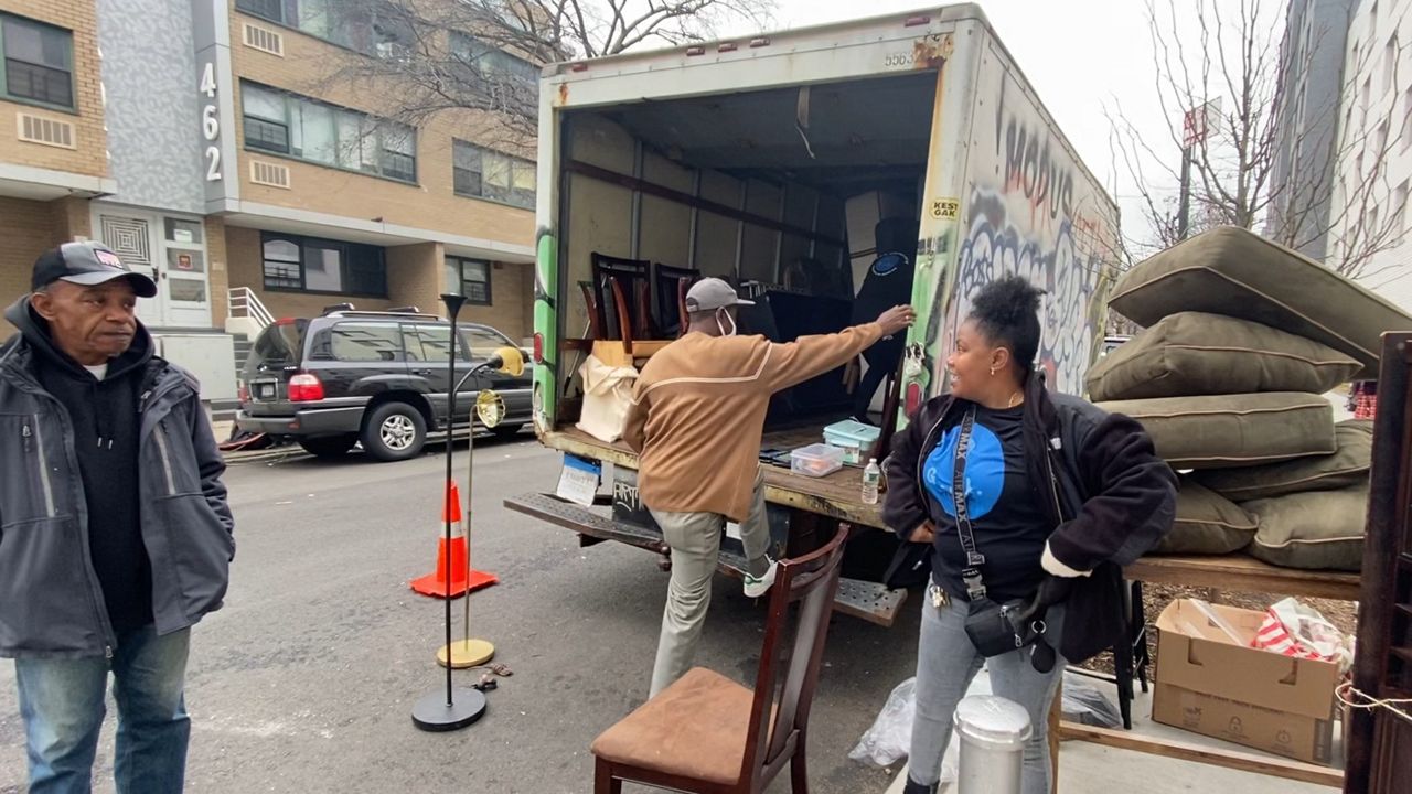 Vanessa Santiago and a volunteer pictured unloading furniture from a van with recipient Keith Hunter on the left standing with hands in his pockets.