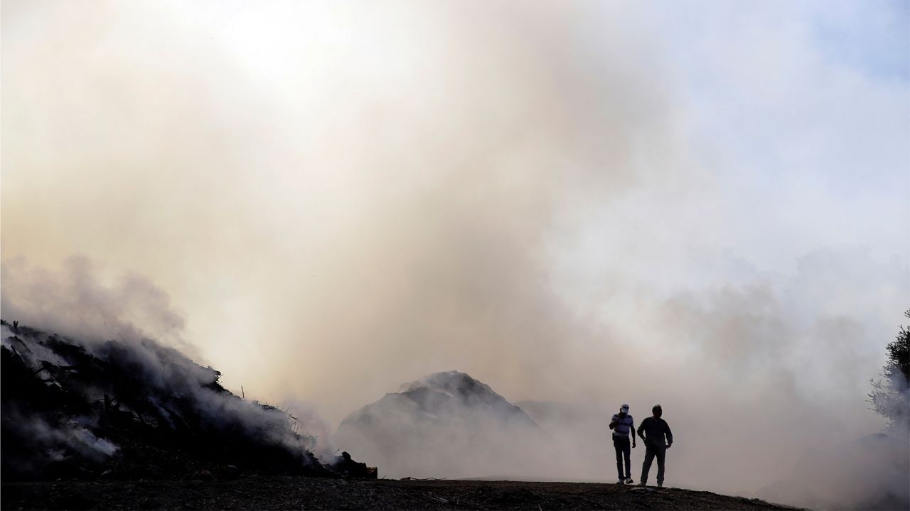 Two men walks along a dirt road as smoke from a wildfire fills the air Saturday, Oct. 12, 2019, in Newhall, Calif. (AP Photo/Marcio Jose Sanchez)