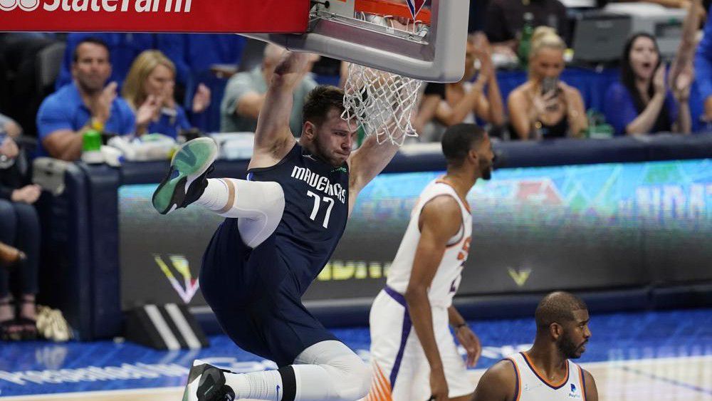 Dallas Mavericks guard Luka Doncic (77) hangs on the rim over Phoenix Suns guard Chris Paul, right, after scoring during the second half of Game 6 of an NBA basketball second-round playoff series, Thursday, May 12, 2022, in Dallas. (AP Photo/Tony Gutierrez)