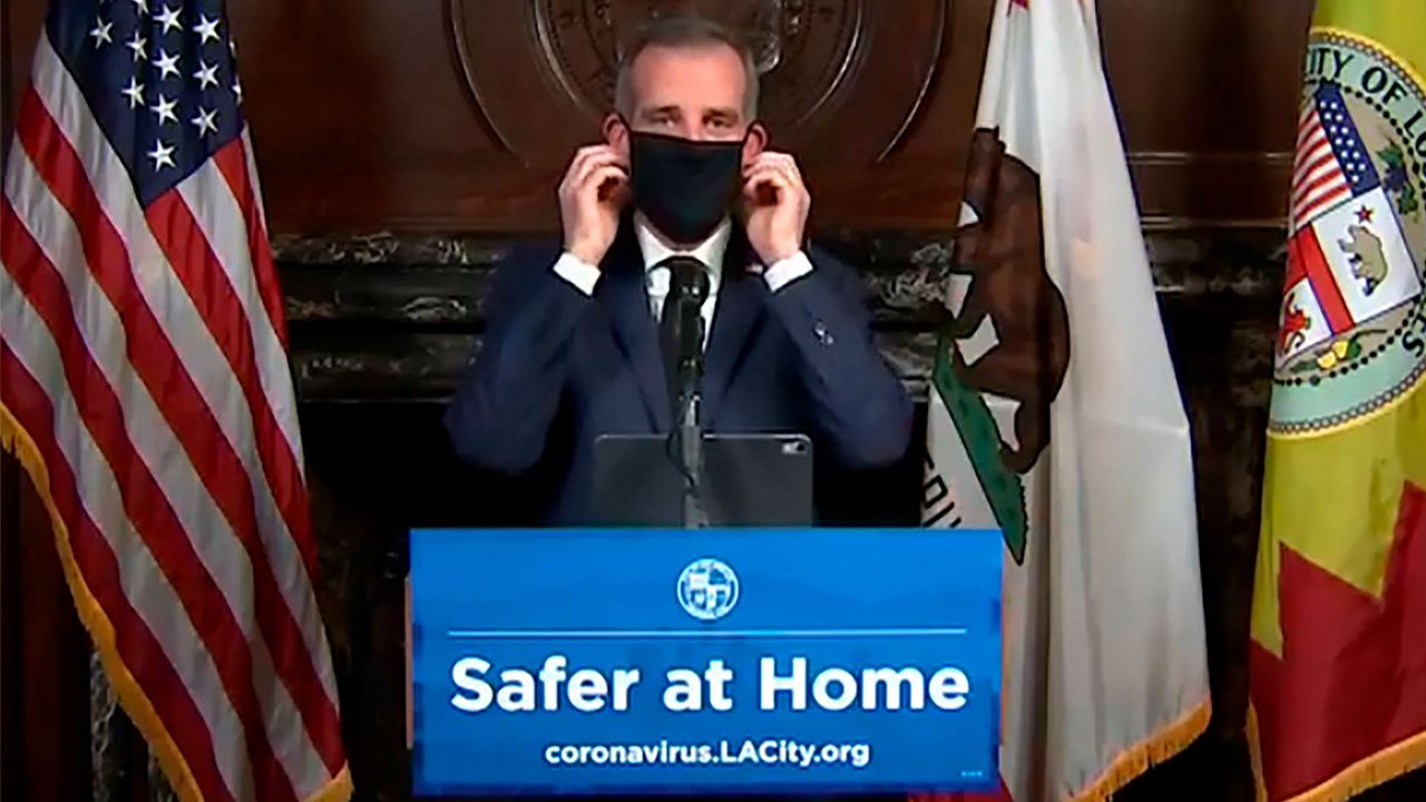 This still image taken from a live stream provided by Office of Mayor Eric Garcetti showing Los Angeles Mayor Garcetti displaying putting on a protective face mask during his daily news conference in Los Angeles on Wednesday, April 1, 2020. Garcetti has recommended that the city's 4 million people wear masks when going outside amid the spreading coronavirus. (Office of Mayor Eric Garcetti via AP)
