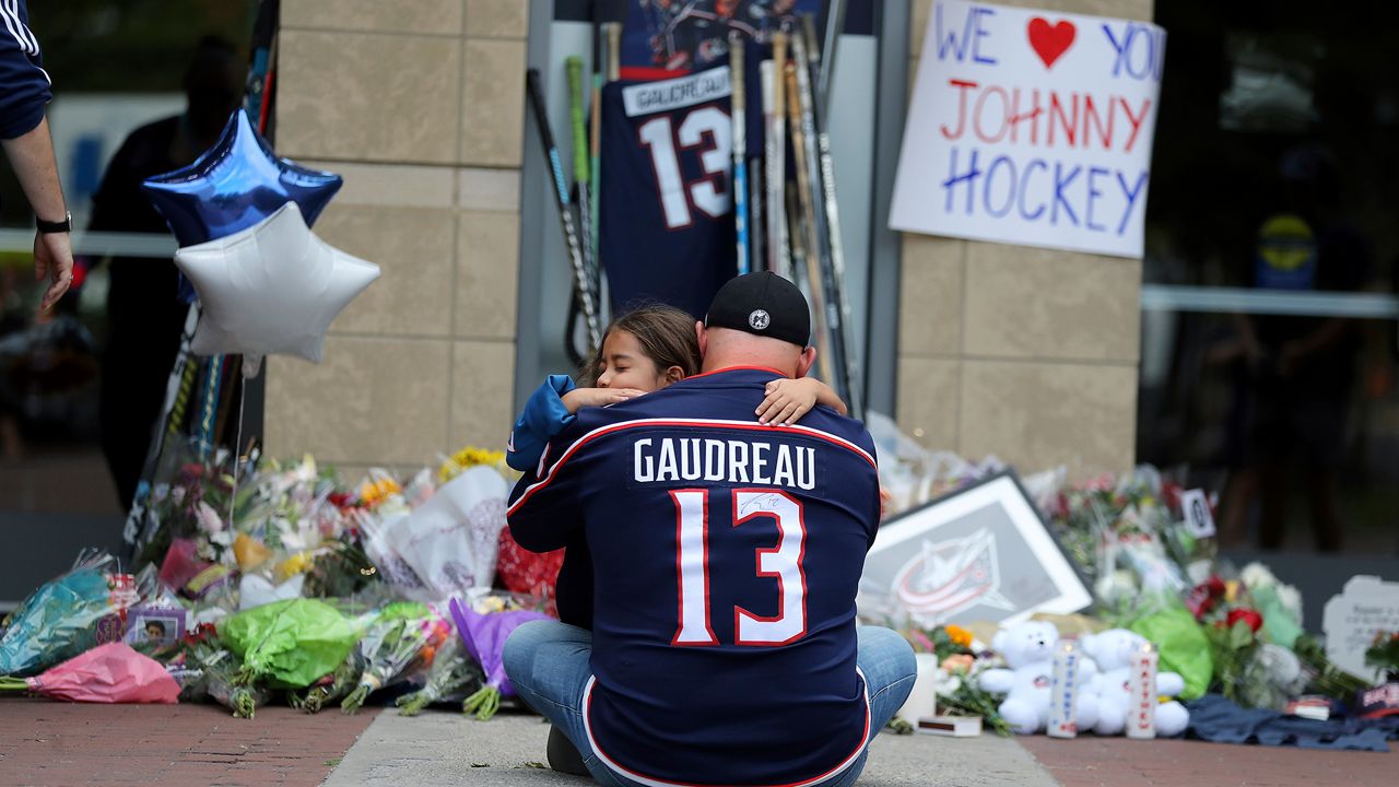 Shiloh Rivera, facing, mourns with Hylas Stemen of Columbus, at the makeshift memorial set up by fans for Blue Jackets hockey player Johnny Gaudreau in Columbus, Ohio, Friday, Aug. 30, 2024. Gaudreau, along with his brother Matthew, was fatally struck by a motorist while riding his bicycle on Thursday. (AP Photo/Joe Maiorana)