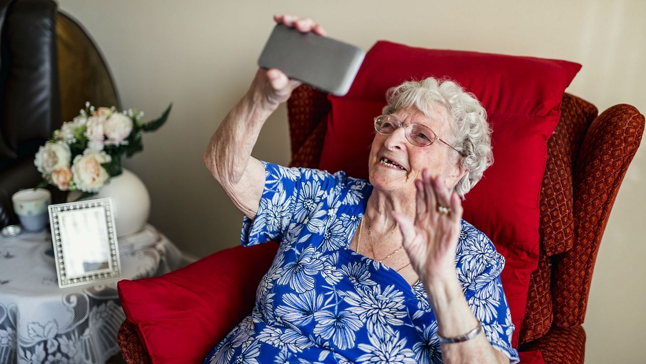 Stock image of a woman holding a cell phone and waving. (Getty Images/SolStock)