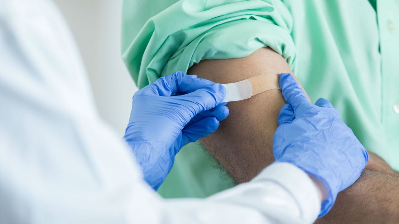 Stock image of a pharmacist placing a bandage on customer's arm. (Getty Images)