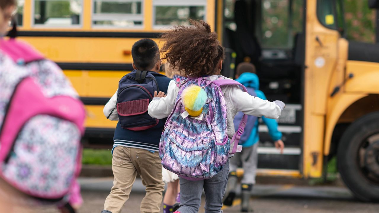 A multi-ethnic group of elementary age children are getting on a school bus. The kids' backs are to the camera. They are running towards the school bus which is parked with its door open. It's a rainy day and the kids are wearing jackets, rain boots and backpacks. (Photo: Getty)