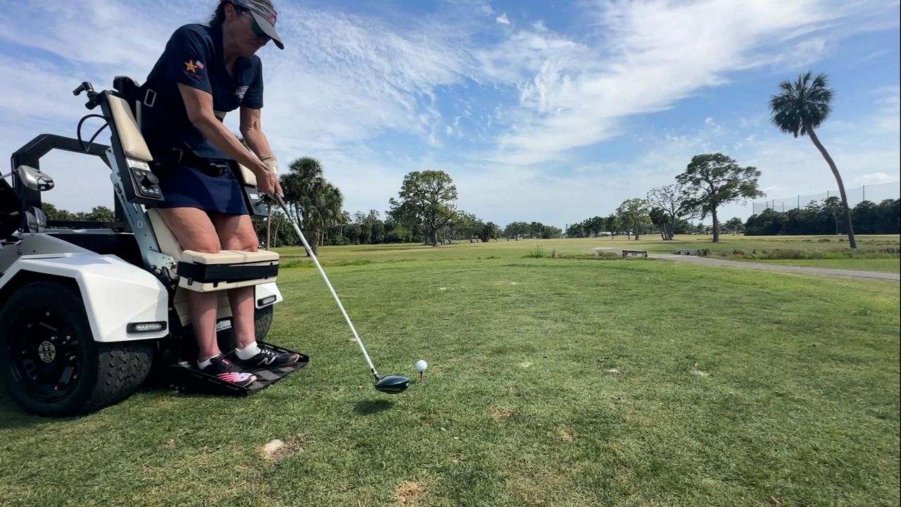 Karen Atkinson takes a swing at a golf ball while using a VertaCat to be in an upright position. (Spectrum News)