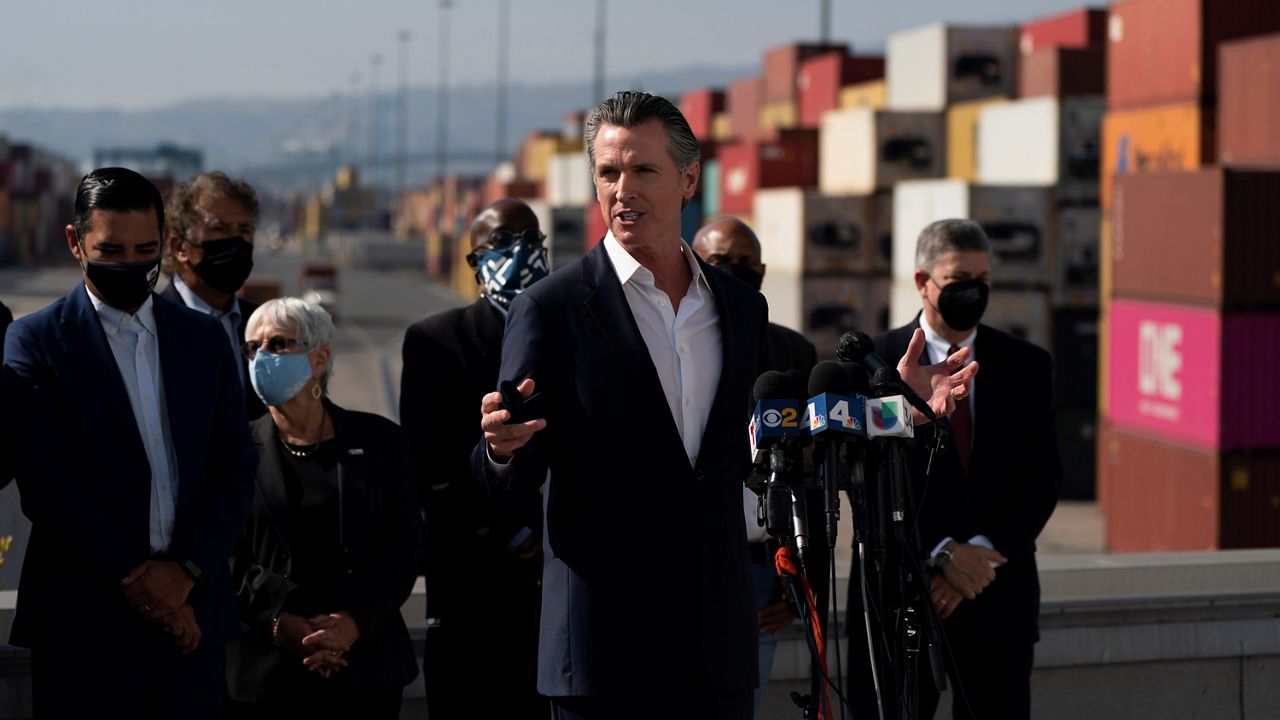 California Gov. Gavin Newsom, center, speaks during a news conference as containers are stacked up in the yards at the Port of Long Beach in Long Beach, Calif., Wednesday, Nov. 17, 2021. (AP Photo/Jae C. Hong)