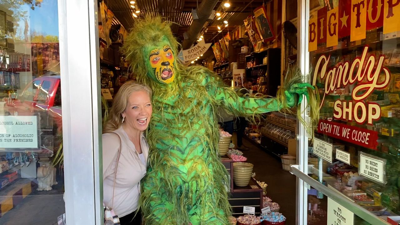 The Grinch standing with a fan in the doorway of a candy shop