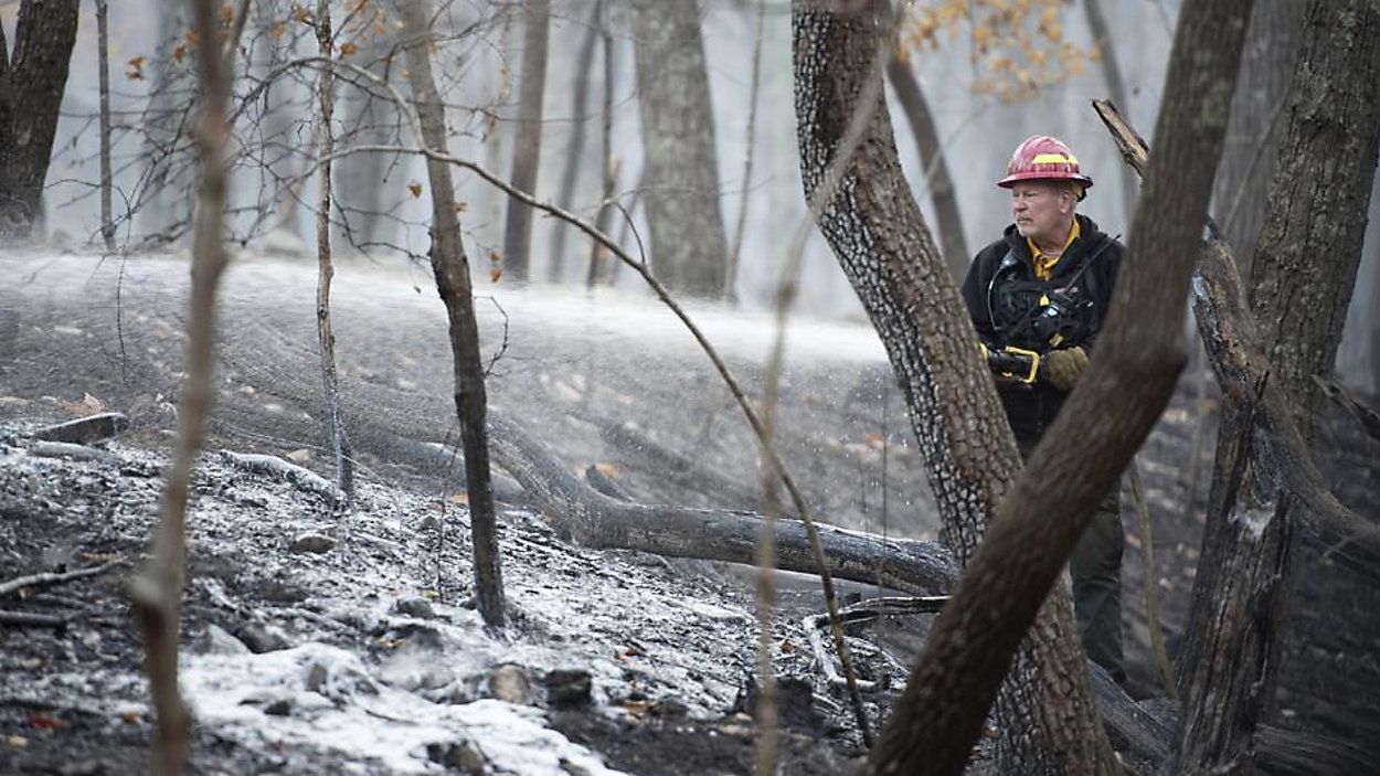 A firefighter with the N.C. Forest Service sprays remaining hot spots from the wildfire at Pilot Mountain State Park that caused damage to over 1,000 acres by Tuesday, Nov. 30, 2021, in Pinnacle, N.C. (Allison Lee Isley/The Winston-Salem Journal via AP)