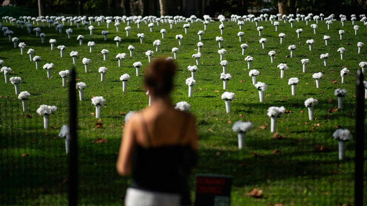 A woman looks at vases of white flowers that are part of an installation of 1,050 representing the lives lost by gun violence in New York in 2020.  (AP Photo/Eduardo Munoz Alvarez)