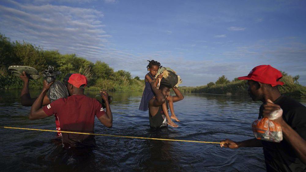 A man carries a little girl, who is clutching her Barbie doll, over the Rio Grande river toward Del Rio, Texas, early Wednesday, Sept. 22, 2021, as other migrants return to Ciudad Acuna, Mexico, some to avoid possible deportation from the U.S. and others to load up with supplies. (AP Photo/Fernando Llano)