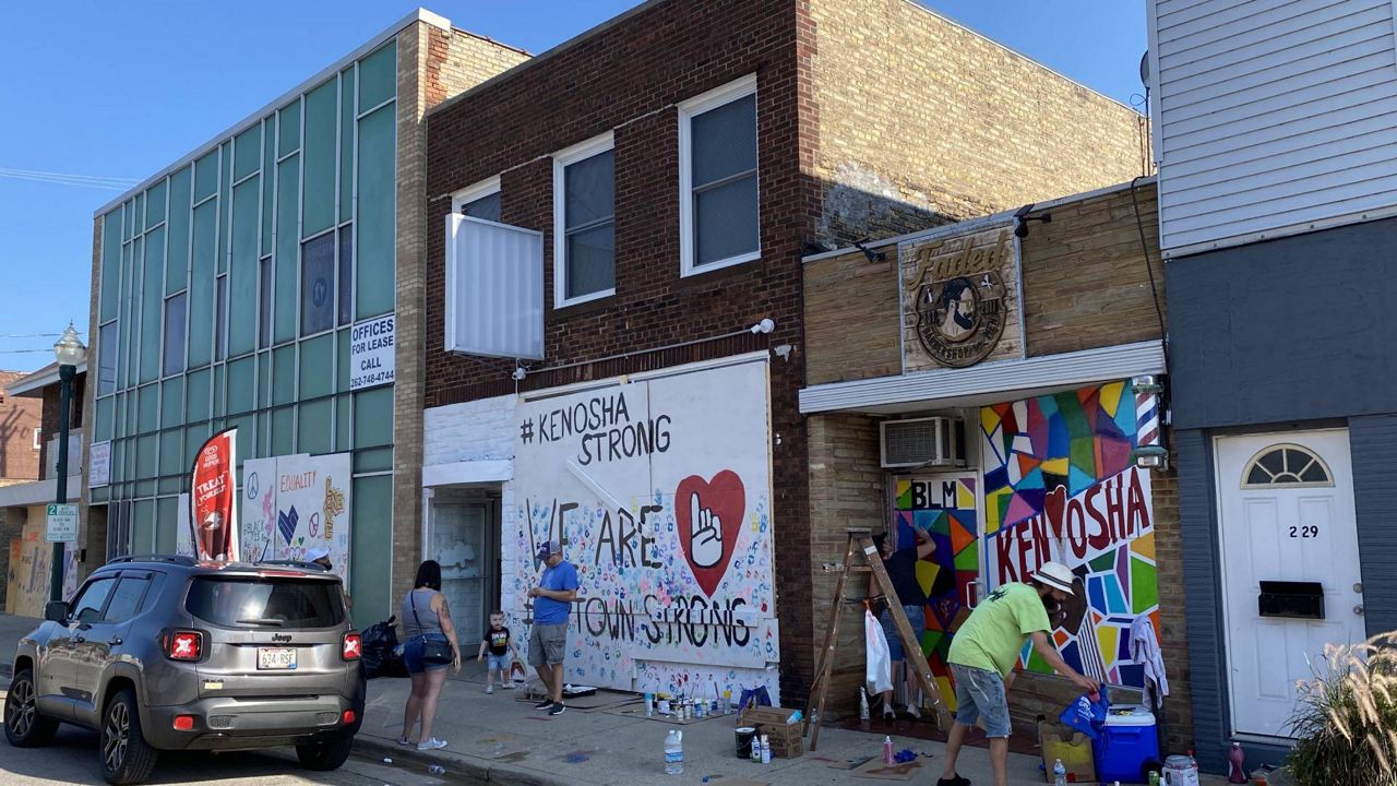 Volunteers help paint the plywood covering broken windows on 63rd Street in Uptown, Kenosha.