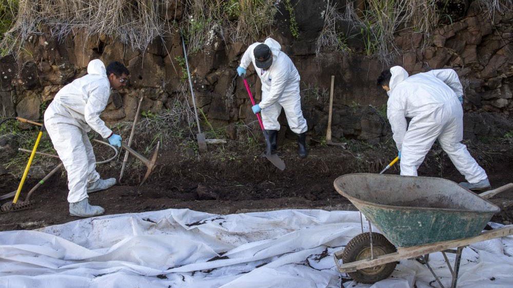 Navy employees use tools to relocate contaminated soil onto a wheelbarrow. (Photo courtesy of U.S. Navy)