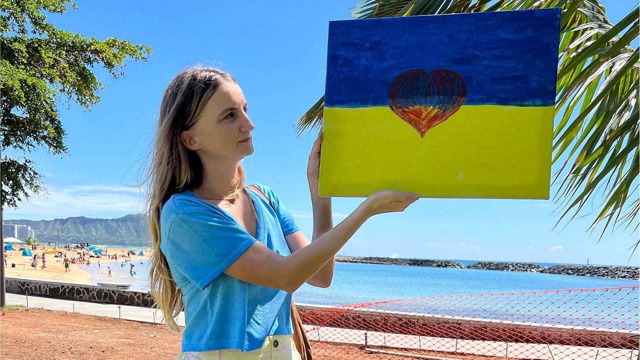 Olga Sousa stands with a painted sign that shows the Ukrainian flag with a heart in the center. (Credit: Olga Sousa)