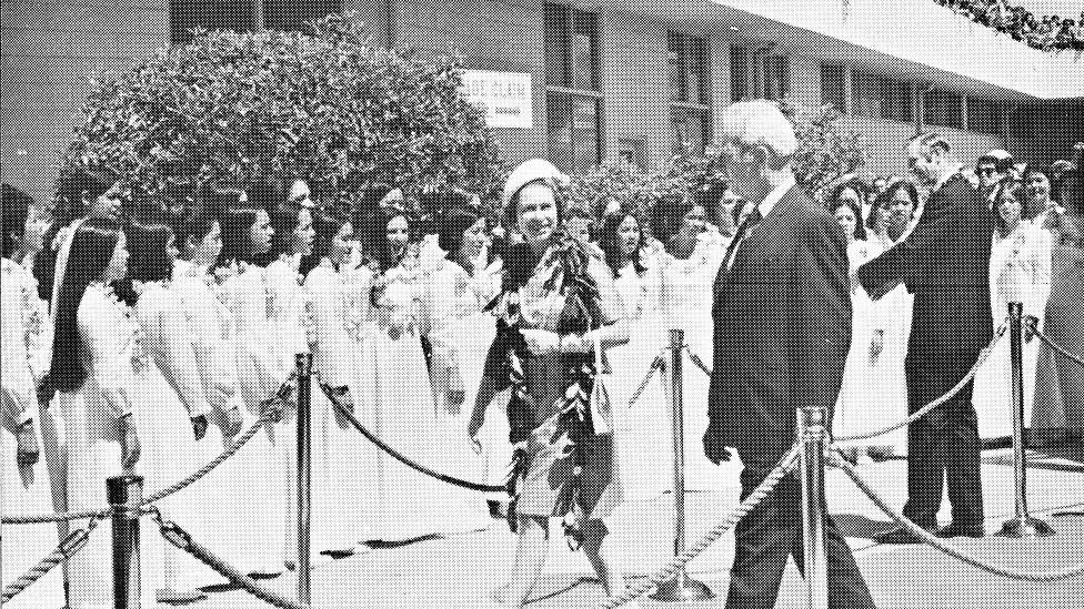 Draped with maile and ilima lei, Queen Elizabeth II walks with Gov. John Burns as the Concert Glee Club sings in the background. (Courtesy Kamehameha Schools)