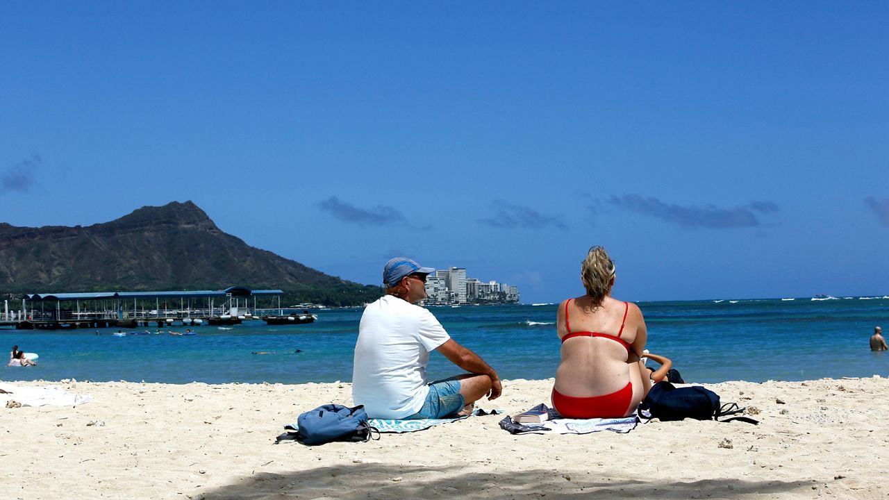 Brett Walsh, left, and Emma Yates, right, tourists from Australia, sit on Waikiki Beach in Honolulu, Monday, May 23, 2022. (AP Photo/Caleb Jones)