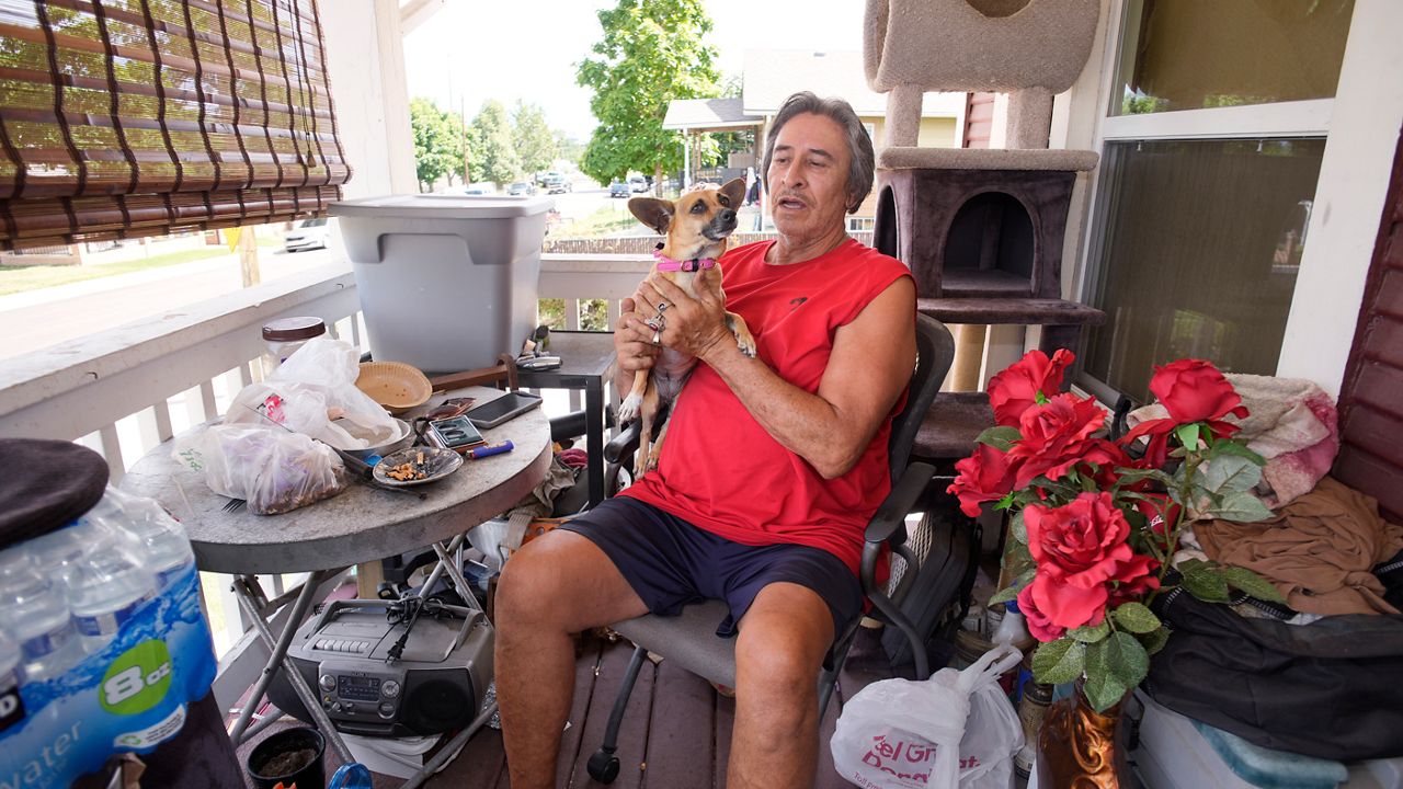 Ben Gallegos sits on the porch of his family's home in the Globeville neighborhood with his dog, Coca Smiles, as the daytime high temperature soars toward triple digits, Thursday, July 27, 2023, in north Denver. Gallegos has taken several measures to keep his home cool in spite of lacking central air conditioning. (AP Photo/David Zalubowski)