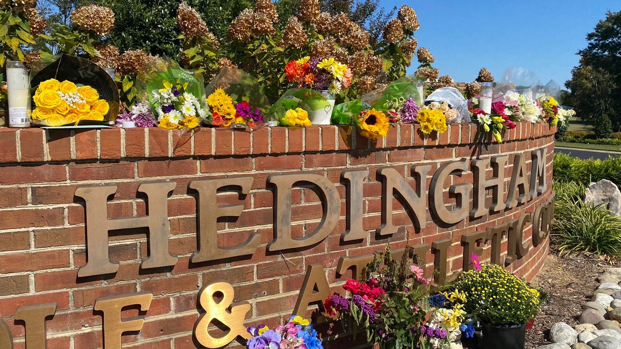 Flowers and candles adorn the entrance of the Hedingham Golf Club on Saturday. The collection has grown since Thursday's deadly mass shooting to span the length of the brick wall. (Spectrum News 1/Josh Conner)