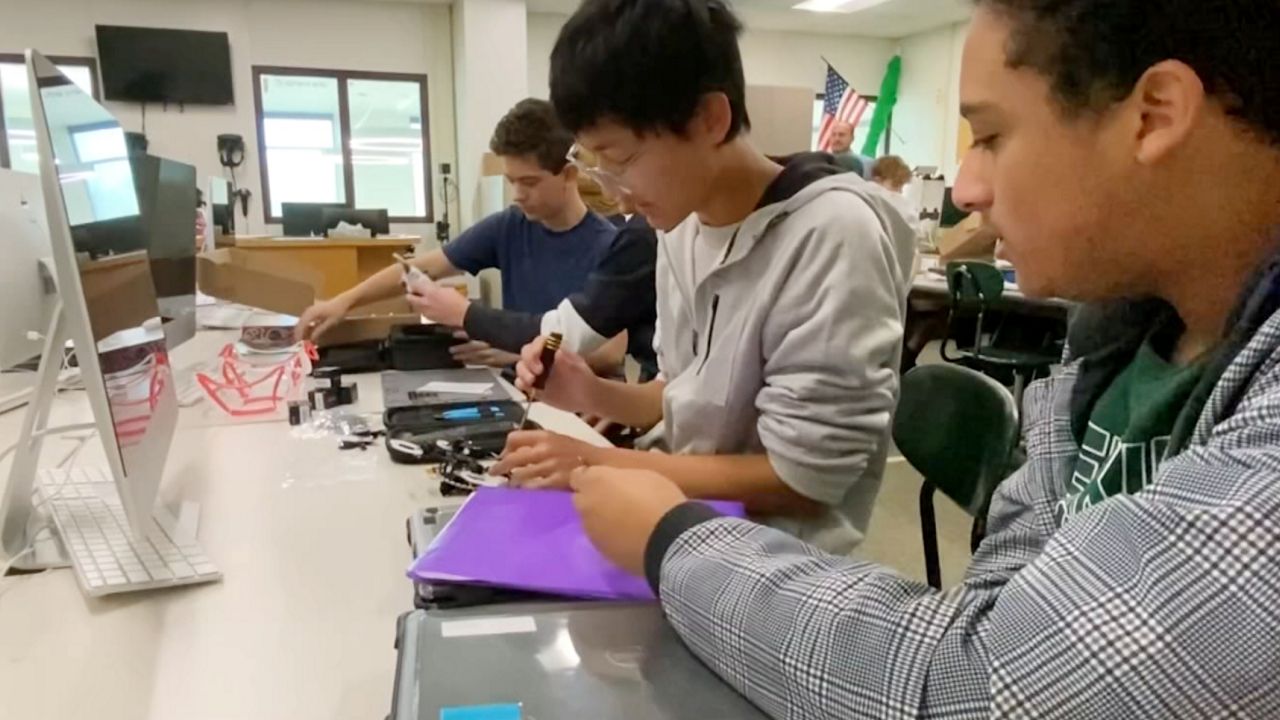 students in high school classroom building drones at a desk
