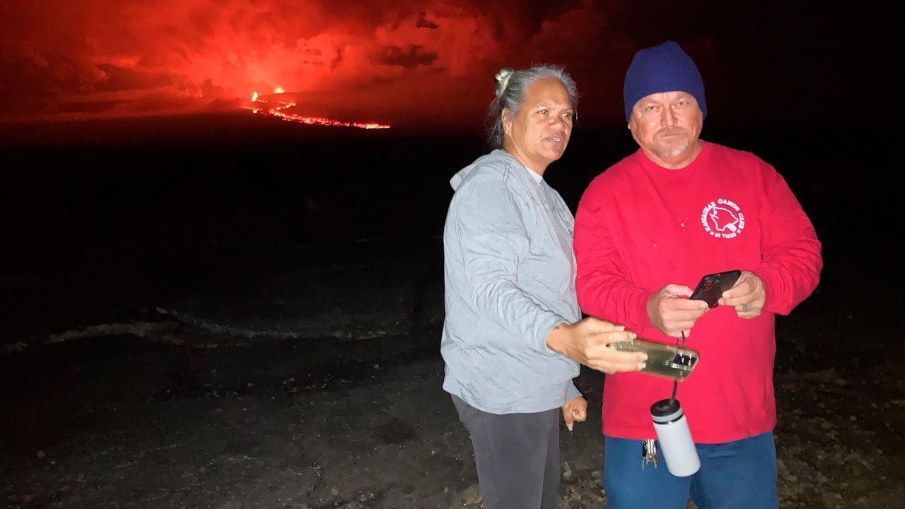 Willette Kalaokahaku Akima-Akau, left, and her husband Eddie Akau stand at a spot overlooking lava flowing from Mauna Loa on Tuesday, Nov. 29, 2022 in Hilo, Hawaii. For Akima-Akau and other Native Hawaiians, the eruption brings deep and personal cultural significance. (AP Photo/Caleb Jones)