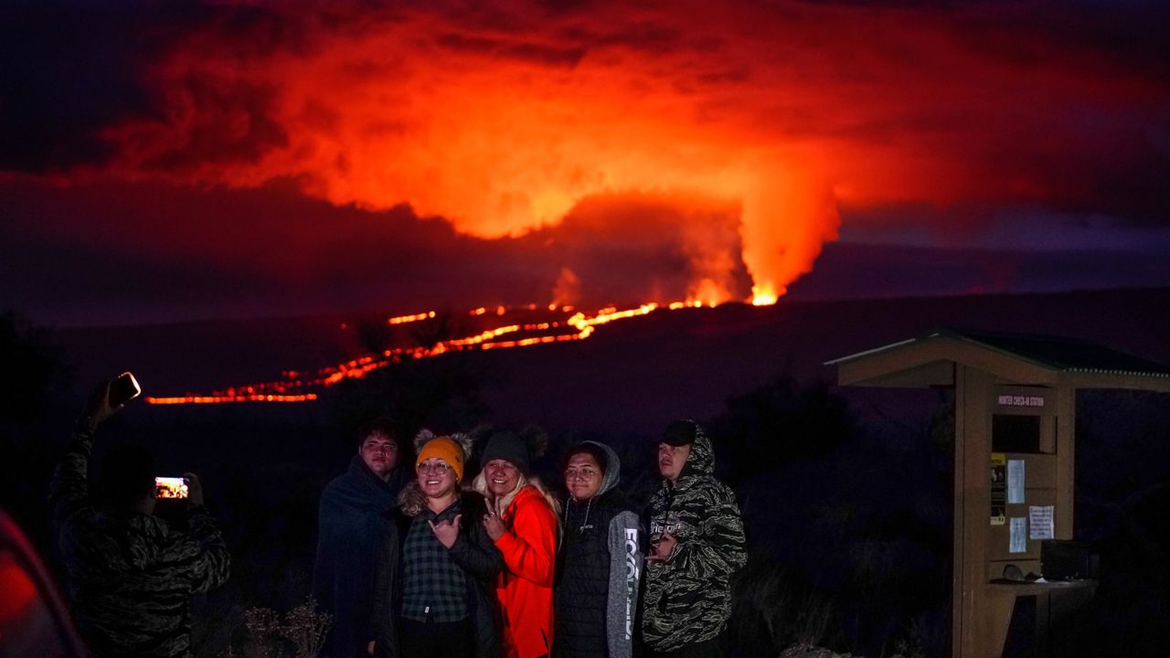 People pose for a photo in front of lava erupting from Hawaii's Mauna Loa volcano Wednesday, Nov. 30, 2022, near Hilo, Hawaii. (AP Photo/Gregory Bull)