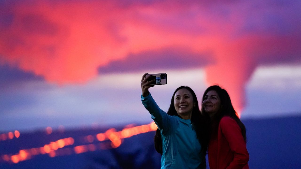 Ingrid Yang, left, and Kelly Bruno, both of San Diego, take a photo in front of lava erupting from Hawaii's Mauna Loa volcano Wednesday, Nov. 30, 2022, near Hilo, Hawaii. (AP Photo/Gregory Bull)