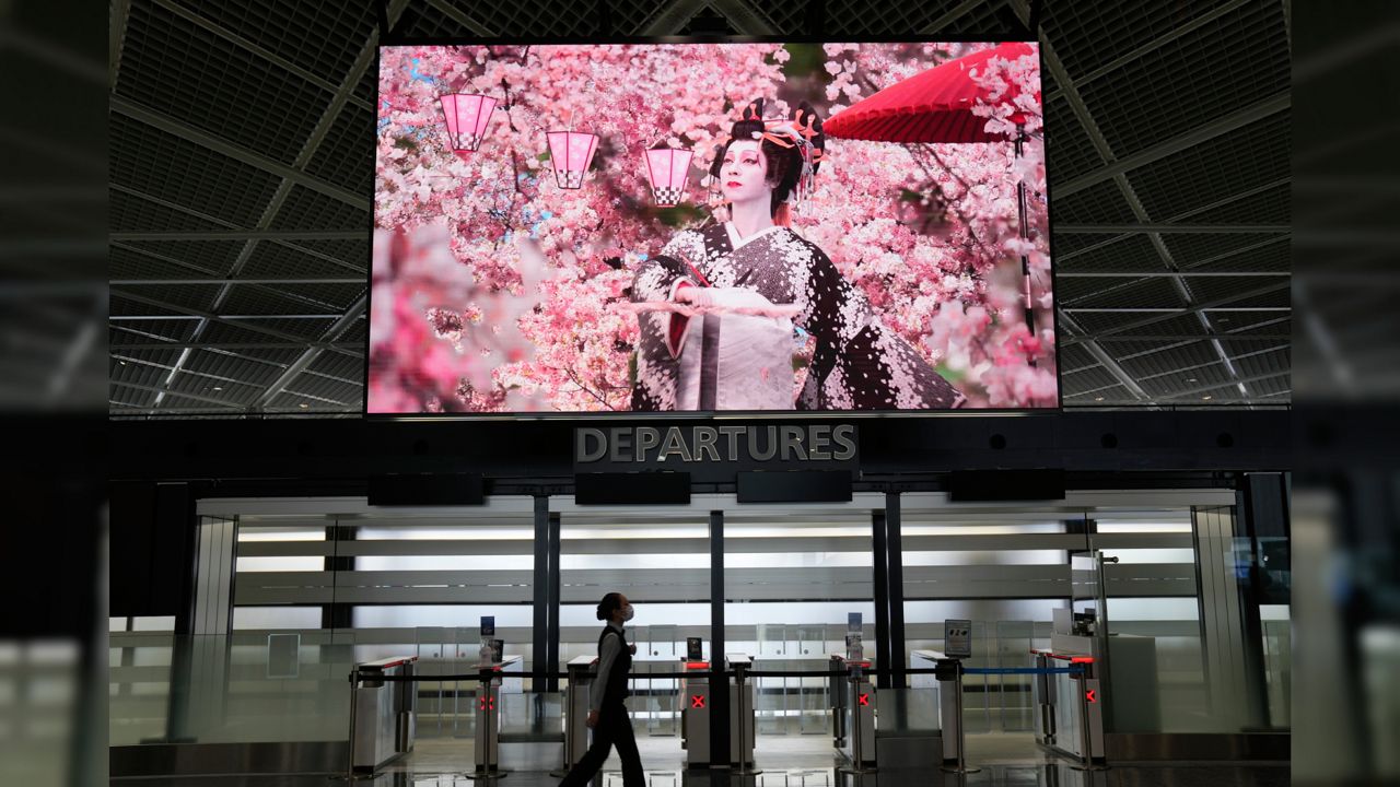 An airline employee walks under promotion video for Japan tourism at Narita international airport in Narita, near Tokyo Friday, June 10, 2022. (AP Photo/Shuji Kajiyama)