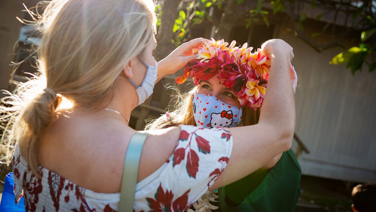 A graduate of the Shidler College of Business at UH Manoa receives a lei from a family member during the Spring 2021 graduation ceremony. UH Manoa is requiring masks for all three of its ceremonies May 13 and 14, and encourages mask wearing when giving lei afterwards. (Shidler College of Business)