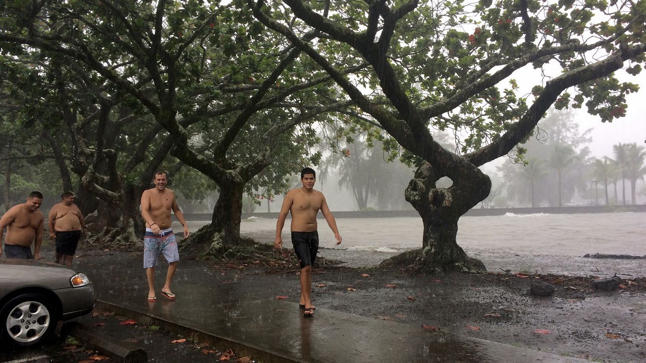 A group of men walk in the rain along Hilo Bay in Hilo, Hawaii, as Topical Storm Madeline drops rain on Hawaii's Big Island, Wednesday, Aug. 31, 2016. Forecasters downgraded Madeline from a hurricane to a tropical storm as it veered past Hawaii's Big Island, but officials reiterated warnings to prepare for heavy rain and strong winds. (AP Photo/Audrey McAvoy)