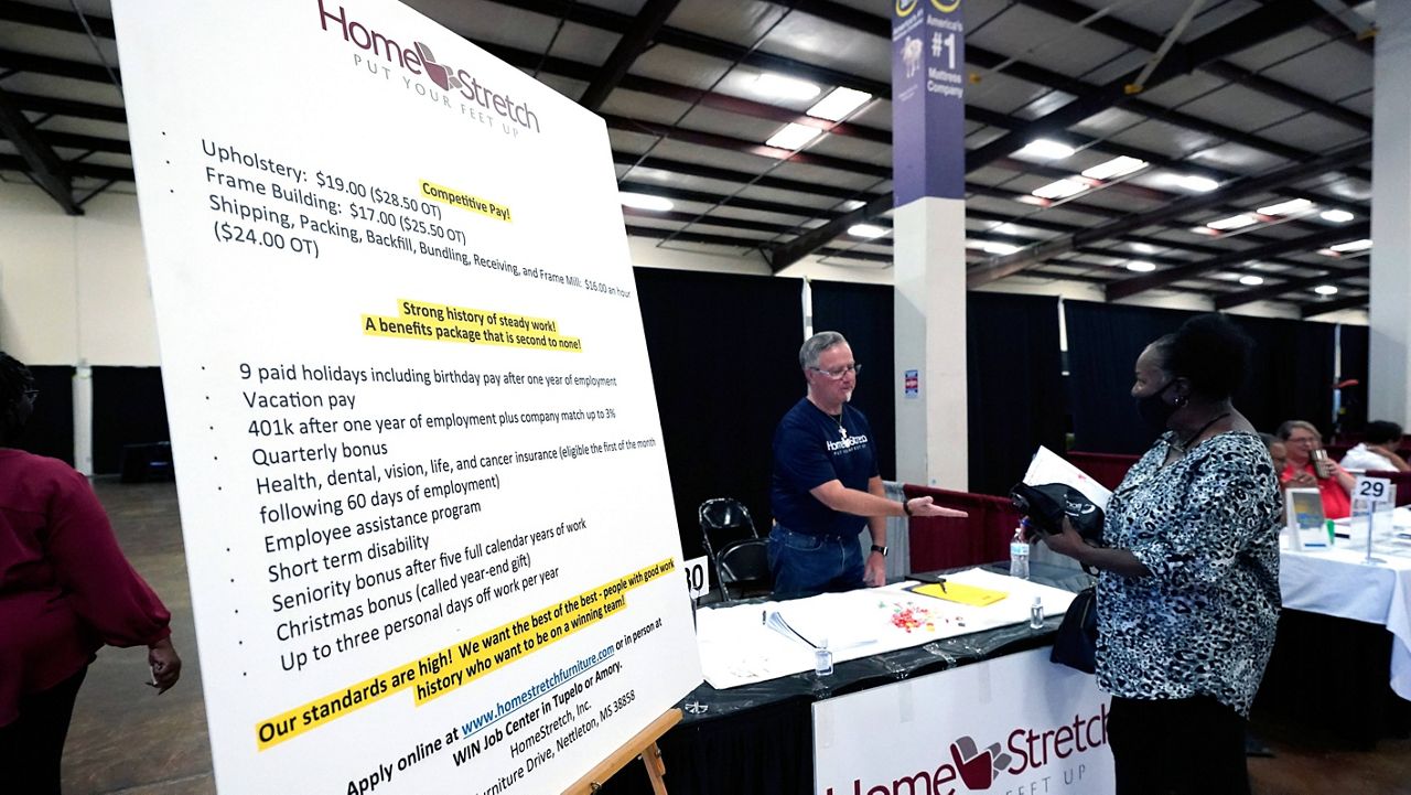 A list of benefits flanks Jon Stembridge, center, a human resource and safety manager with HomeStretch, a domestic manufacturer of upholstered reclining furniture, as he welcomes a potential applicant to his company's recruiting booth during the Lee County Area Job Fair in Tupelo, Miss., on Oct. 12. (AP Photo/Rogelio V. Solis) 