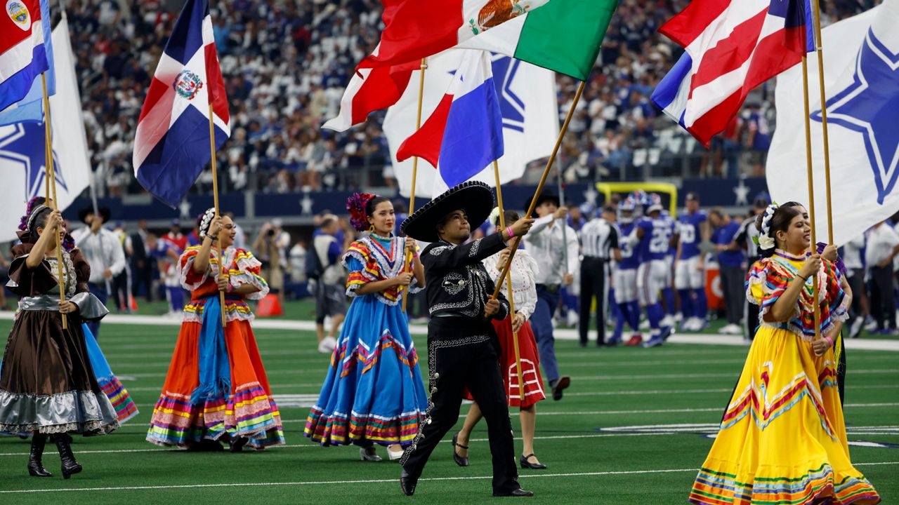 Participants carry flags from several different countries during a pregame ceremony celebrating hispanic heritage month before an NFL football game between the New York Giants and Dallas Cowboys in Arlington, Texas, Sunday, Oct. 10, 2021. (AP Photo/Ron Jenkins)