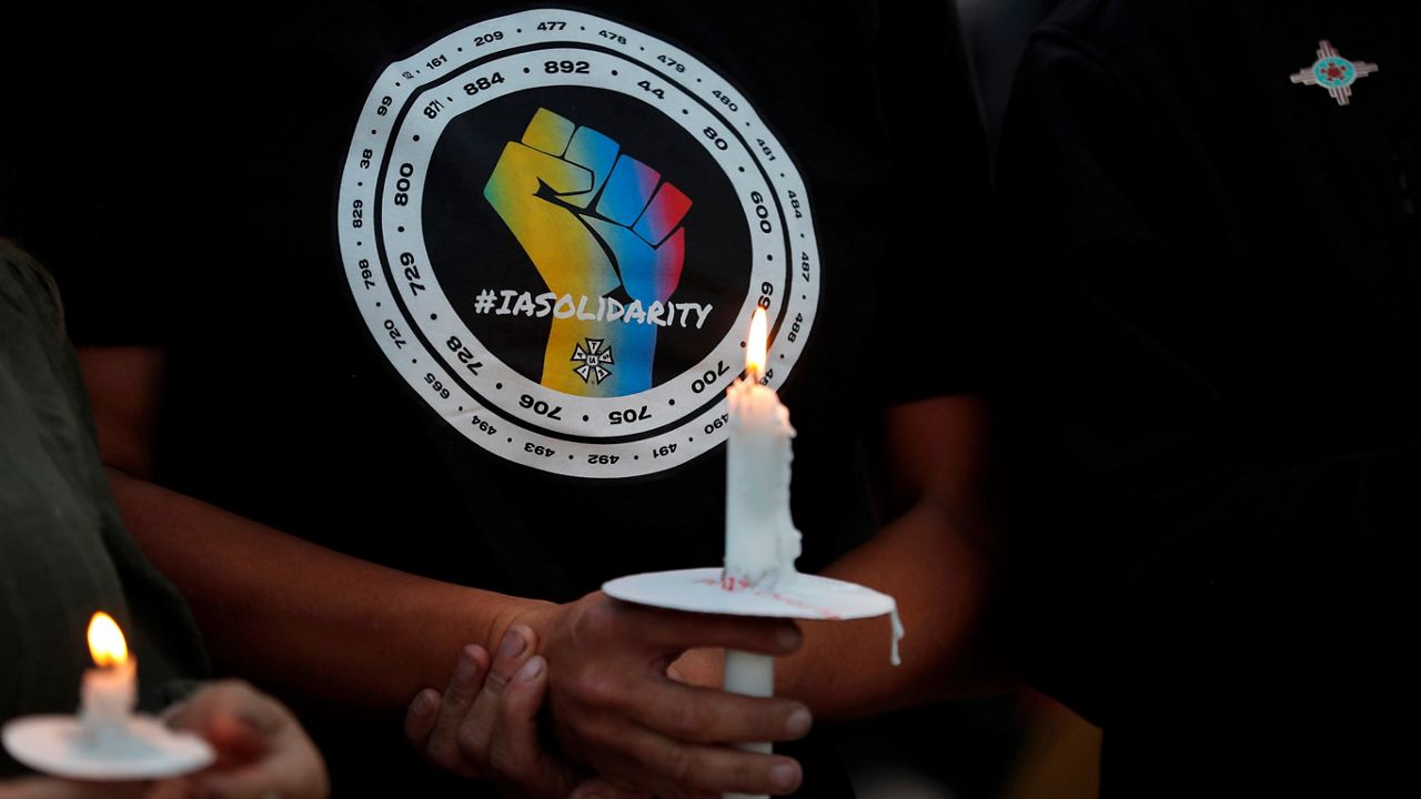 Movie industry worker Hailey Josselyn, wearing a t-shirt of the International Alliance of Theatrical Stage Employees (IATSA), holds a candle during a vigil to honor cinematographer Halyna Hutchins in Albuquerque, N.M., on Oct. 23, 2021. (AP Photo/Andres Leighton, File)