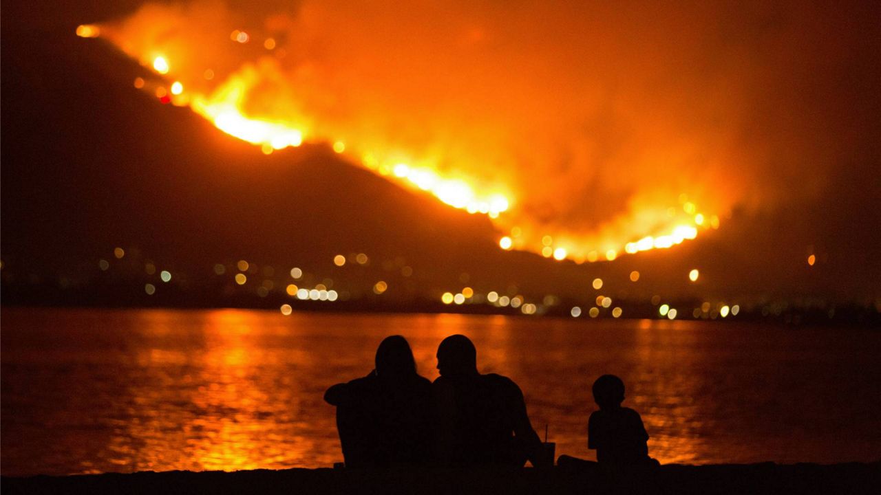 In this Aug. 9, 2018, file photo, a family sits along the shore of Lake Elsinore as they watch the Holy Fire burn in the distance in Lake Elsinore, Calif. (AP Photo/Patrick Record)