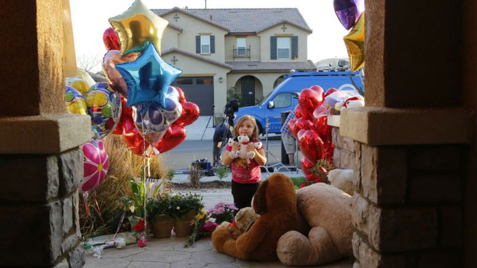 Neighbor plays with toys after dropping off a couple of her own teddy bears on the porch of a home where police arrested a couple on Sunday accused of holding 13 children captive in Perris, Calif. (AP Photo/Damian Dovarganes)