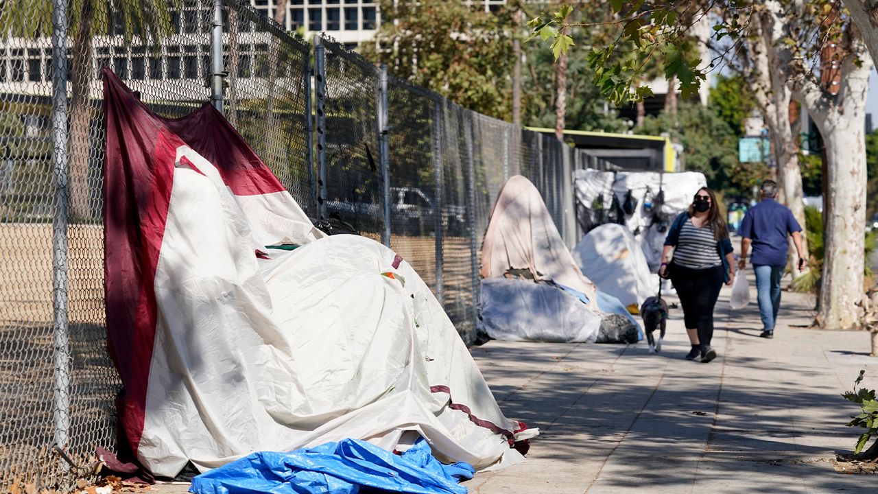 Pedestrians walk past a homeless encampment just outside Grand Park, Wednesday, Oct. 28, 2020, in Los Angeles.  (AP Photo/Chris Pizzello)